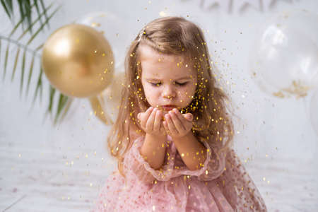 happy child girl with long hair in pink dress blowing confetti and celebrating her birthdayの写真素材
