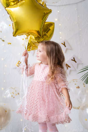 happy little blond girl in pink dress holding balloons and celebrating her birthdayの写真素材