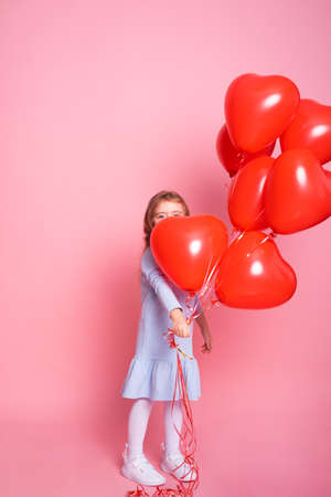 Beautiful child girl with red heart romantic balloons on pink background. Concept of Valentines dayの写真素材