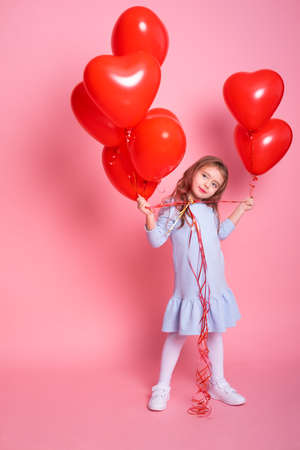 Beautiful child girl with red heart romantic balloons on pink background. Concept of Valentines dayの写真素材