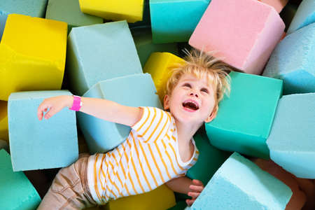 Cute child boy plays with soft cubes in the dry pool in play center