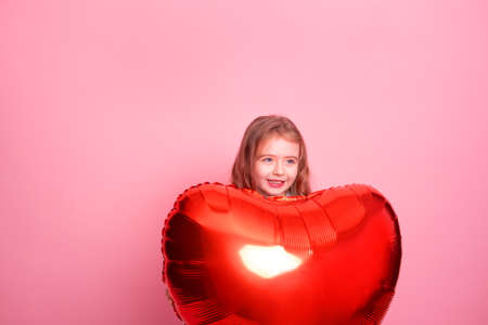 Beautiful child girl with red heart balloon on pink background celebrating Valentine dayの写真素材