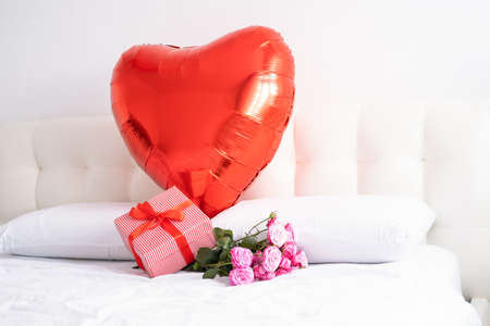 Valentine day background. Big red heart balloon , gift box and bouquet pink roses on white beddingの写真素材