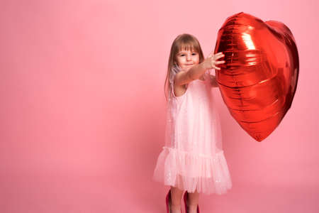 Beautiful child girl with big red heart balloon on pink background celebrating Valentine dayの写真素材