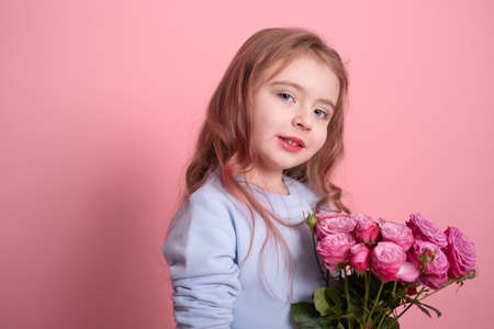 portrait of cute little girl in blue dress holding bouquet of pink roses on pink backgroundの写真素材