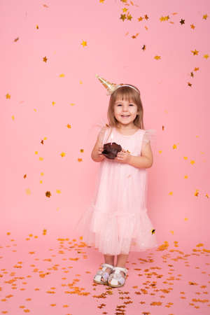 Funny child girl in dress with birthday cupcake with candle on pink backgroundの写真素材