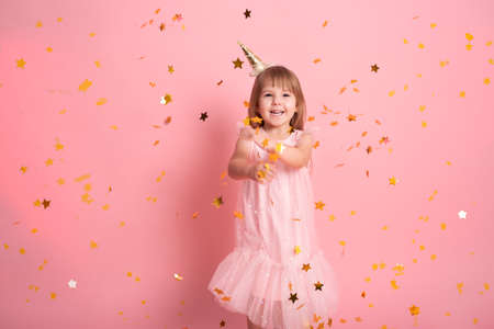 happy child girl in dress having fun with confetti and celebrating her birthday on pink backgroundの写真素材