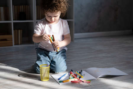 curly child girl drawing with colored markers sitting on floor in living room at home