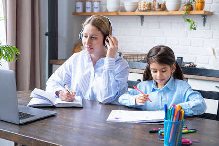 woman in headphone having online lesson education using laptop. kid girl drawing sitting next to herの写真素材