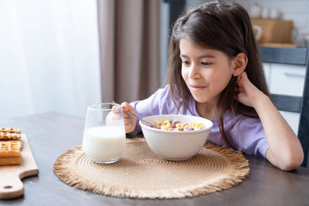 Happy arab child girl having breakfast colorful cereal with milk at home on the morningの写真素材