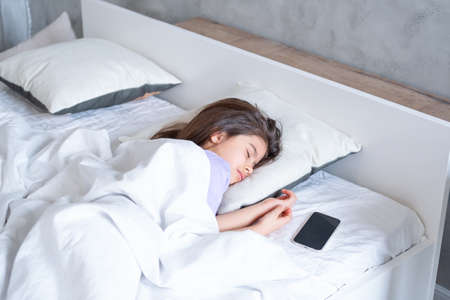 cute arab child girl with long hair sleeping on white bedding at home, phone are near herの写真素材