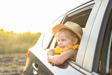 happy child girl in straw hat looking out of a car window in summer nature at sunsetの写真素材