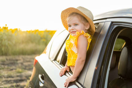 happy child girl in straw hat looking out of a car window in summer nature at sunsetの写真素材