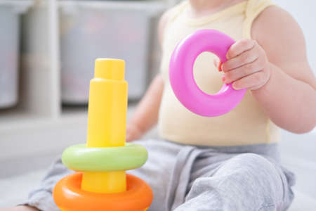 Cute baby girl playing in colorful pyramid on floor at home. Early childhood development