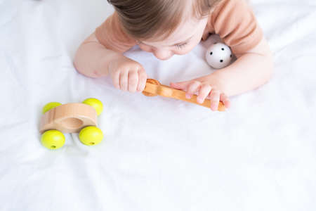 baby girl with blue eyes in brown bodysuit playing with wooden toys on white bedding on bedの写真素材