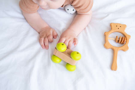 baby girl with blue eyes in brown bodysuit playing with wooden toys on white bedding on bedの写真素材
