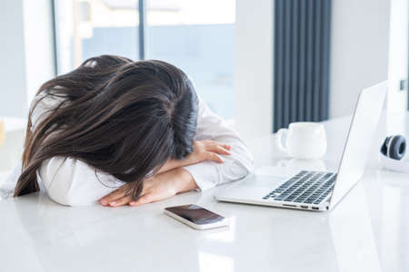 Young asian tired business woman with long hair working at laptop in bright home officeの写真素材