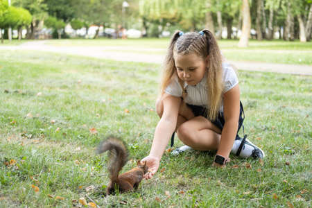 happy schoolgirl in uniform with backpack feeds a squirrel in the park on her way to schoolの写真素材