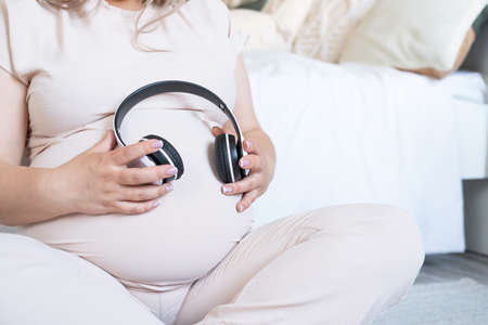 pregnant woman with big belly applying headphones to her belly for prenatal music stimulationの写真素材