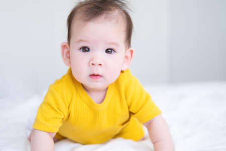 healthy asian baby girl 5 months in yellow bodysuit on bed on white beddingの写真素材