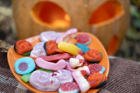 Halloween background. scary candies on a plate near pumpkin with candle