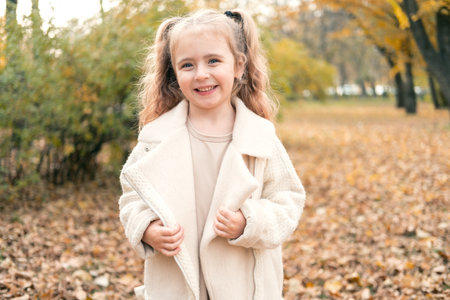 portrait of smiling beautiful little girl in stylish clothes in nature in autumn parkの写真素材