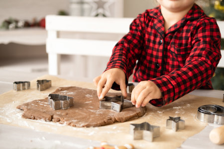 little kid girl in red pajama cooking festive gingerbread in christmas decorated kitchen. christmas cookiesの写真素材
