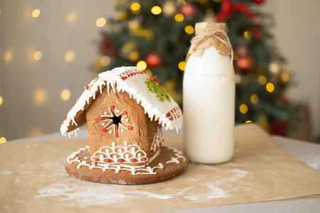 gingerbread house and bottle of milk on table on background of Christmas tree
