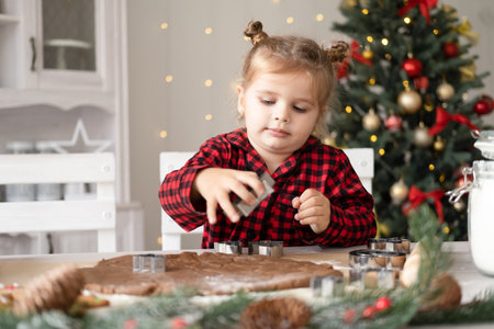 little girl in red pajama cooking festive gingerbread in christmas decorated kitchenの写真素材