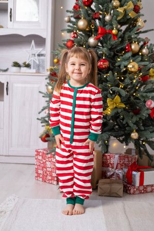 cute little child girl in Christmas pajamas with gift boxes under Christmas tree at home.の写真素材