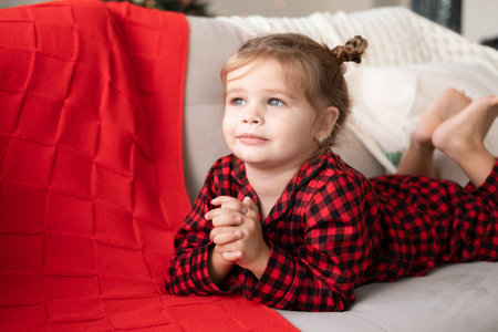 cute little girl in red Christmas pajama smiling lying on couchの写真素材