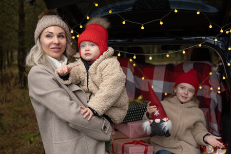 Happy family of mom and two kids with Christmas gift boxes sitting in christmas decorated carの写真素材