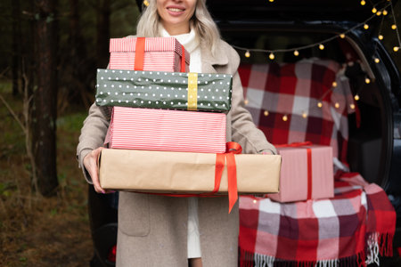 Young woman in warm cozy clothes with Christmas gift boxes near carの写真素材