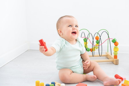 cute baby girl in bodysuit playing with colorful wooden toys on white room.の写真素材