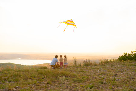 Happy man and children, father and sons, with kite in nature at sunset.の写真素材