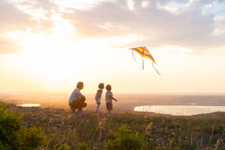 Happy man and children, father and sons, with kite in nature at sunset.の写真素材