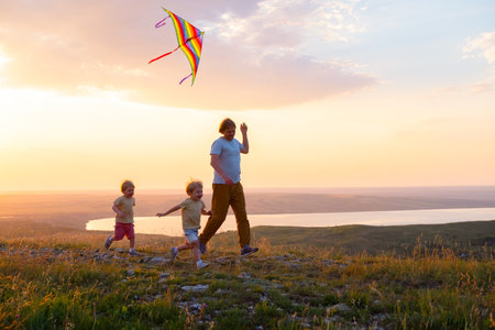 Happy man and children, father and sons, with kite in nature at sunset.の写真素材