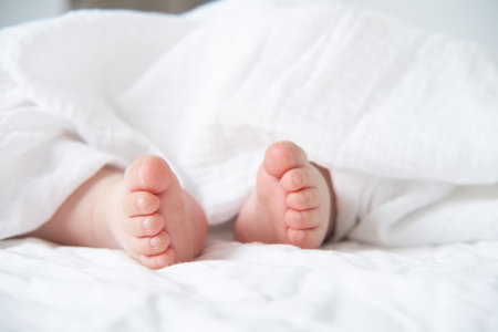 baby bare feet on a white bed with a white blanket.
