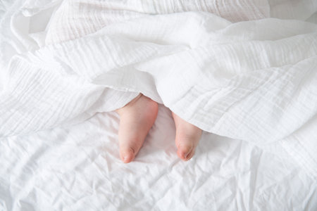 baby bare feet on a white bed with a white blanket.の写真素材
