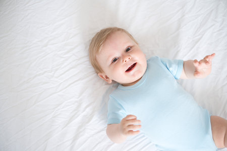 A baby with blonde hair smiling laying on a white bed. top view.の写真素材