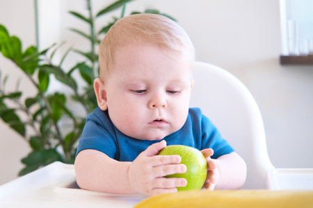 baby eating apple sitting in a high chair.の写真素材