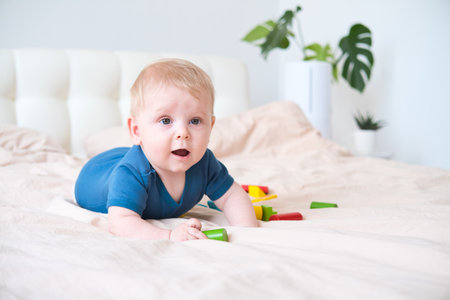 baby boy in blue bodysuit playing with colorful wooden eco toys on bed.の写真素材