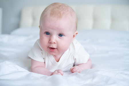cute smiling baby lying on tummy on parent bed.の写真素材