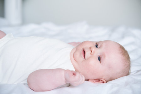 healthy smiling baby lies on his back on bed on white bedding.の写真素材