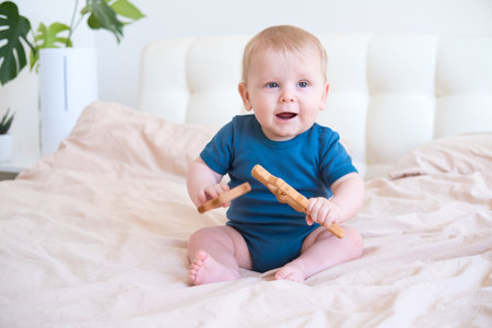baby boy in blue bodysuit playing with wooden eco toys on bed.の写真素材