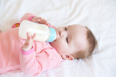 the baby drinks milk from a bottle lying on bed.の写真素材