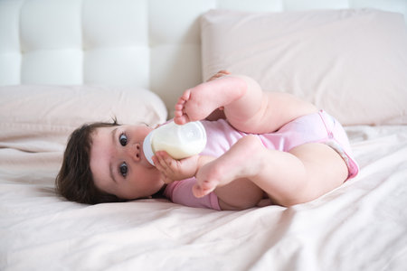 the baby drinks milk from a bottle lying on bedの写真素材