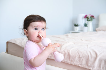 cute smiling baby with plastic bunny toy standing holding on to the bed frame.の写真素材