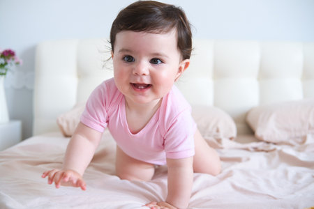 portrait of smiling healthy baby in pink bodysuit on bedの写真素材