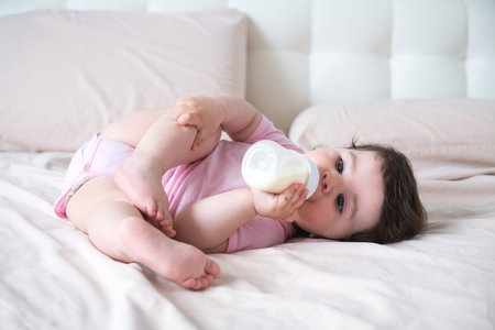 the baby drinks milk from a bottle lying on bed.の写真素材